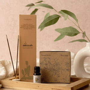 Amayah product packaging with tea tree oil bottle and dhoop sticks on a wooden tray.